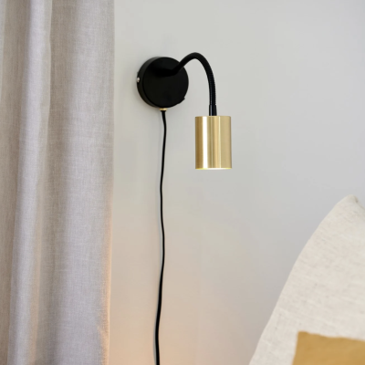 Luz de parede preta e dourada junto a cortina cinza e sofá com almofadas