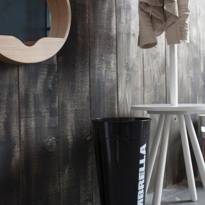 Suporte de metal preto para guarda-chuvas com texto branco junto a parede de madeira