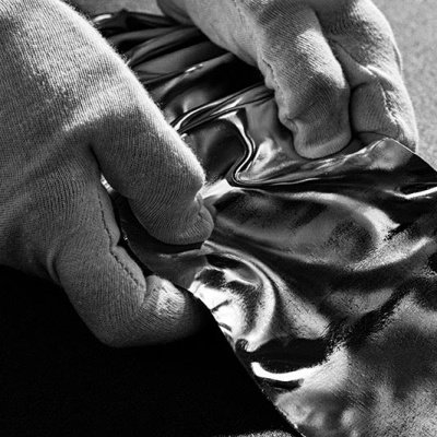 Mãos com luvas a segurar material brilhante e enrugado