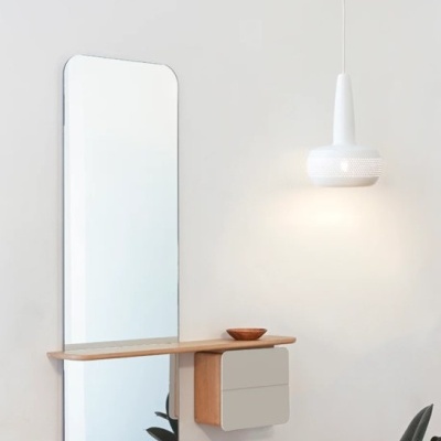Espelho vertical com prateleira de madeira e gavetas cinzentas na parede branca, com luminária pendente branca ao lado