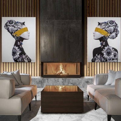 Sala de estar com poltronas bege, lareira com moldura em pedra, mesa de centro em madeira e dois quadros decorativos com perfis femininos e flores