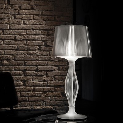 Abajur branco translúcido sobre mesa de vidro junto a parede de tijolos