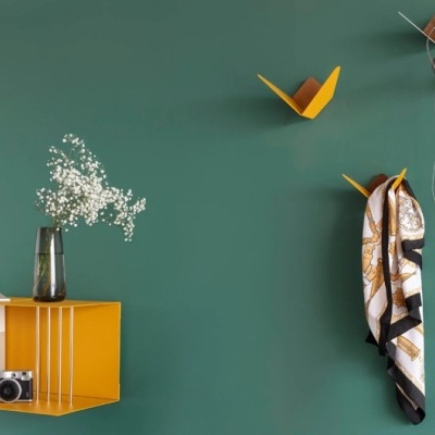 Estante amarela com objetos decorativos numa parede verde