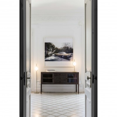 Sala com mesa de madeira escura, duas luminárias de pé e pintura de carro clássico na parede.