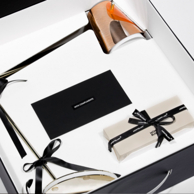 Caixa de presente preta aberta com relógio, caixa pequena branca com fita preta, envelope preto e outro item com bracelete preto dentro