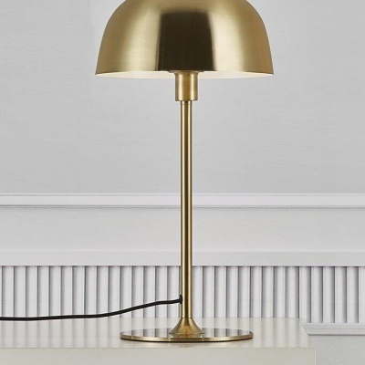 Candeeiro de mesa dourado com cúpula arredondada sobre mesa branca