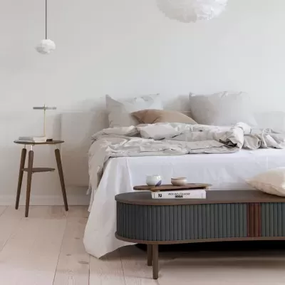 Quarto minimalista com cama branca, mesa de apoio de madeira e mesa de centro escura oval.
