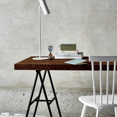 Mesa de trabalho com tampo castanho e cadeira branca junto a uma parede cinzenta