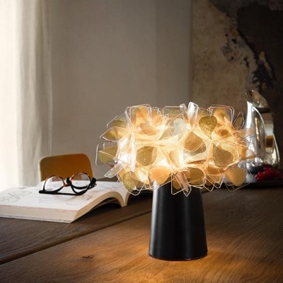 Luminária de mesa com cúpula dourada em tecido e base preta sobre mesa de madeira com livro e óculos