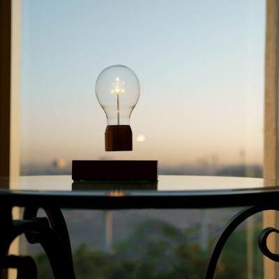 Lâmpada LED flutuante com base em madeira sobre mesa de vidro e janela ao entardecer