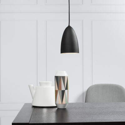 Mesa preta com jarra branca, vaso decorado e lâmpada pendente preta