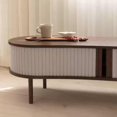 Mesa de centro oval em madeira com detalhes brancos ondulados e objetos em cima