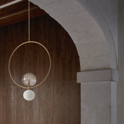 Luminária pendente dourada com duas bolas de luz numa sala com parede de madeira e arco de pedra