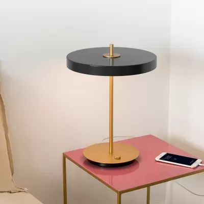 Candeeiro de mesa moderno com base dourada numa mesa rosa ao lado de sofá