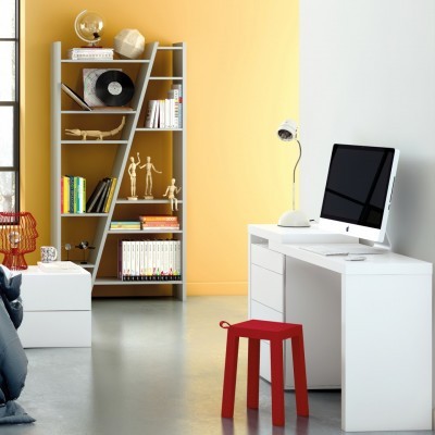 Escritório com escrivaninha branca, computador, banco vermelho e estante cinzenta com livros e decoração.