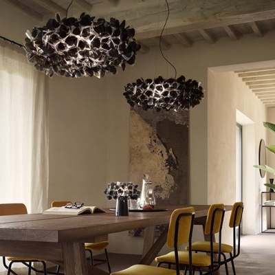 Luminárias pendentes pretas em formato floral sobre mesa de madeira com cadeiras amarelas