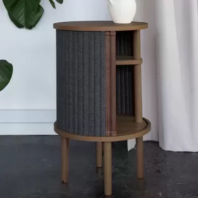 Mesa de apoio redonda em madeira clara com painel lateral em tecido cinza escuro e estante