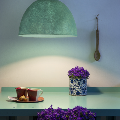 Lustre verde pendente sobre mesa azul com chávenas e vaso de flores roxas