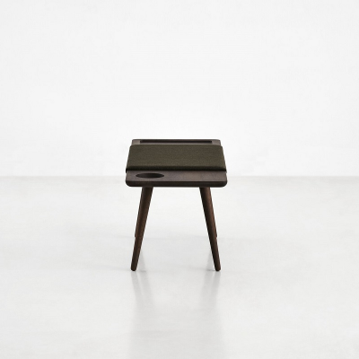 Banco pequeno em madeira escura com três pés, sobre piso branco
