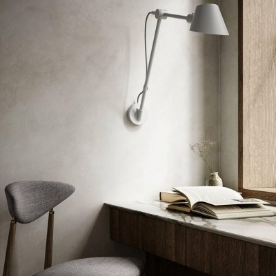 Cadeira cinza em tecido e madeira junto a mesa com tampo branco e candeeiro de parede branco num ambiente minimalista