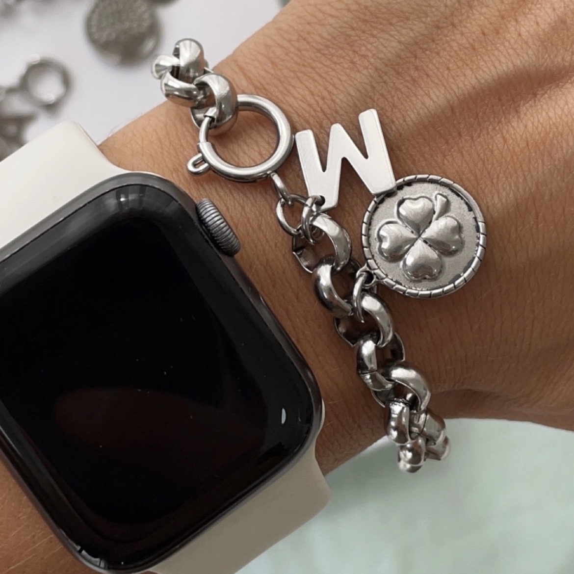 LUCK Pulseira prateada com pendente de trevo e letra W junto a relógio inteligente