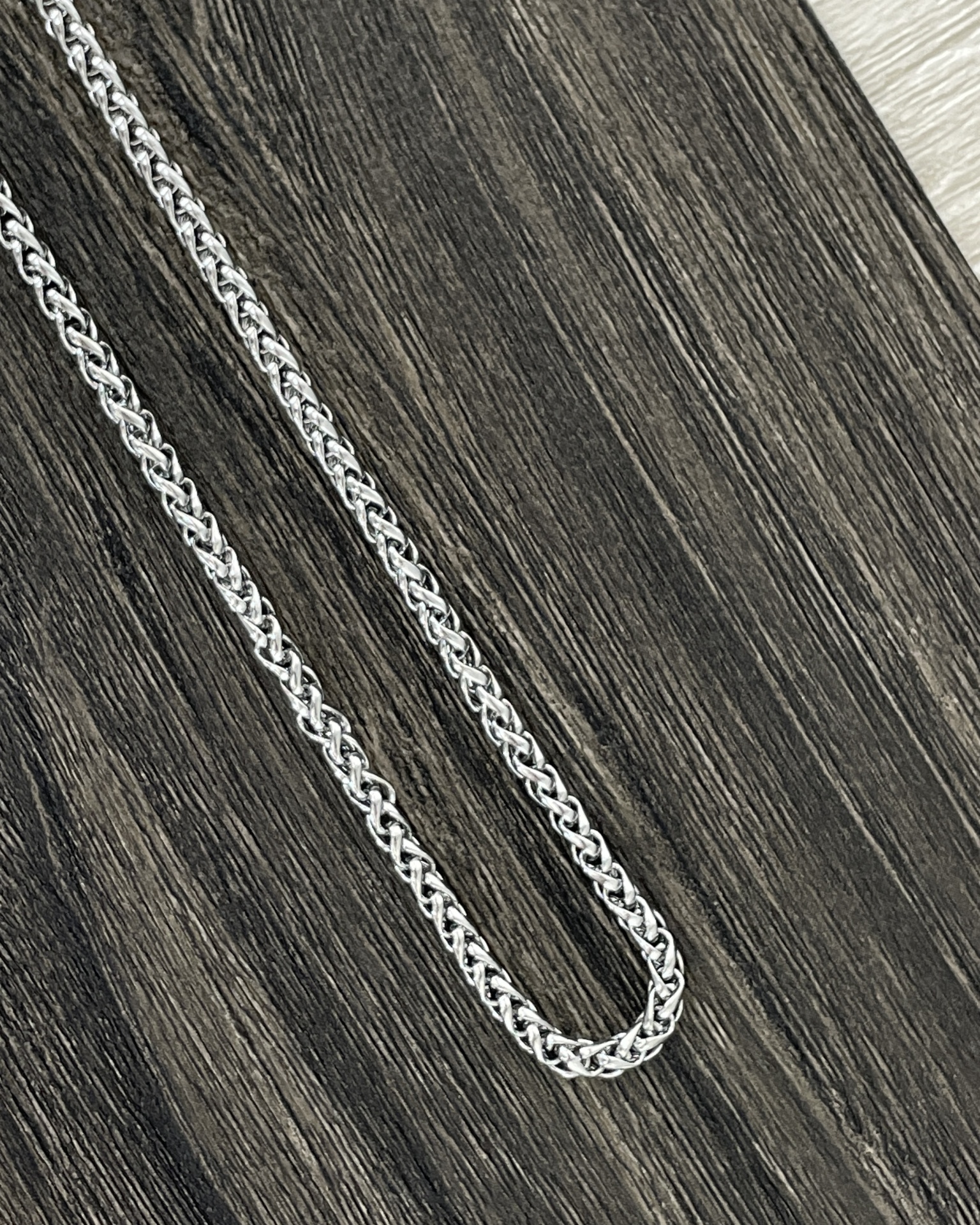 COLARES HOMEM Colar de corrente prateada de padrão entrelaçado sobre superfície de madeira escura