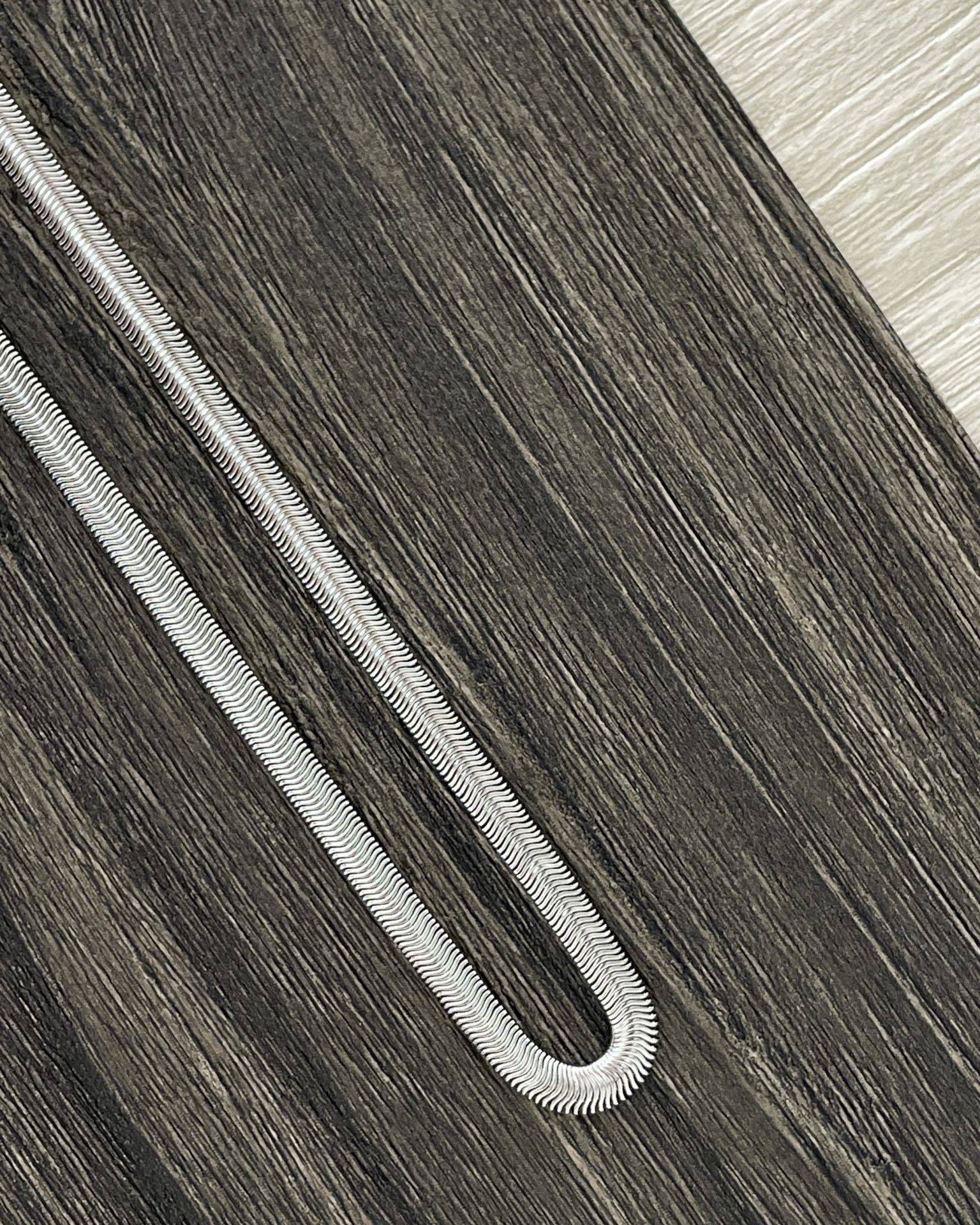 COLARES HOMEM Corrente de prata com padrão texturizado sobre madeira escura