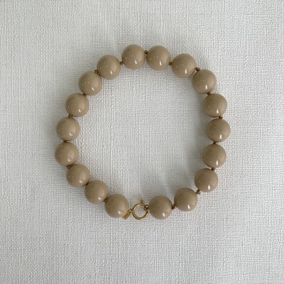 Pulseira bege com esferas lisas e fecho dourado sobre fundo branco texturizado