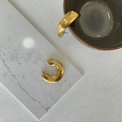 Brincos de argola dourados ao lado e dentro de uma taça cinza em superfície marmoreada