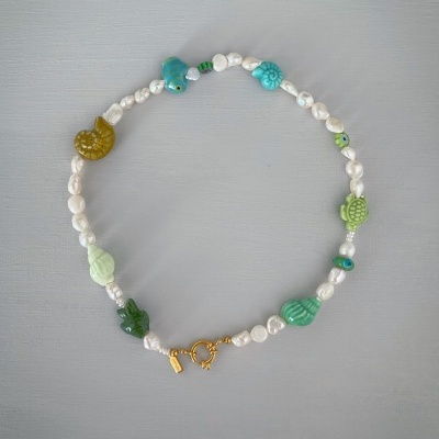 Colar de pérolas com contas decorativas coloridas em formas marinhas e fecho dourado em fundo cinza.