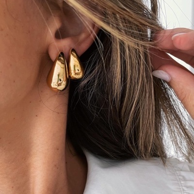 Brincos dourados em formato de gotas usados na orelha de mulher
