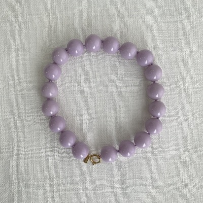 Pulseira lilás com contas redondas e fecho dourado em fundo branco texturado