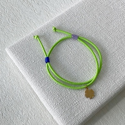Pulseira verde com pendente dourado em forma de flor sobre tecido branco