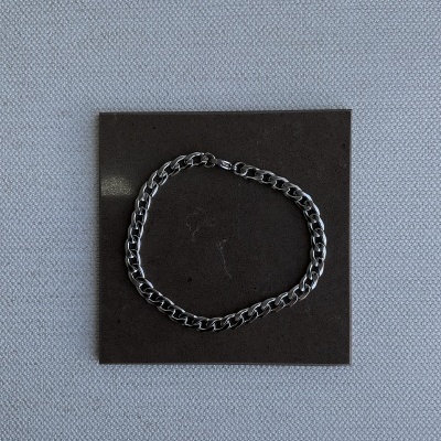 Pulseira prateada de correntes sobre quadro preto em fundo de tecido cinzento