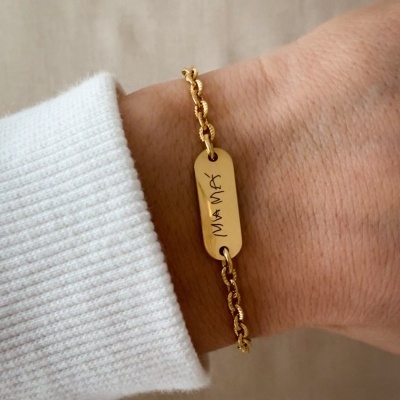 Pulseira dourada com pendente gravado MÃE num pulso com manga branca