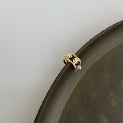 Anel dourado com pérolas branco posicionado na borda de um prato metálico escuro