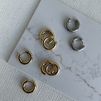 Brincos de argola pequenos dourados e prateados sobre placa branca com padrão mármore