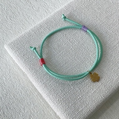 Pulseira de cordão verde claro com pendente dourado em fundo branco texturado