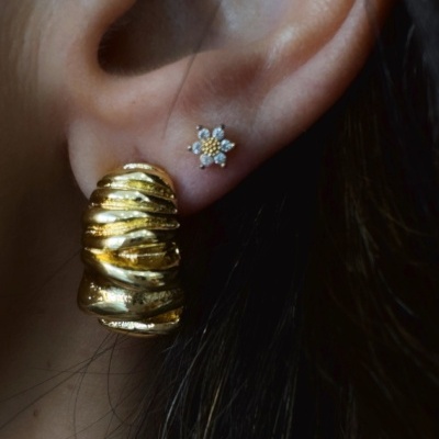 Brincos dourados ondulados e flor com pedras num ouvido.