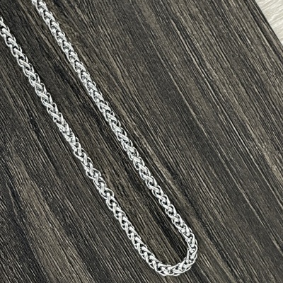 Colar de corrente prateada de padrão entrelaçado sobre superfície de madeira escura