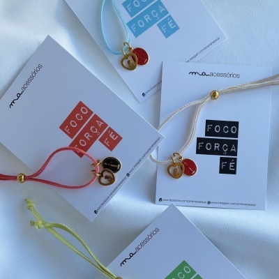 Pulseiras coloridas com pendentes dourados e cartões com texto FOCO FORÇA FÉ