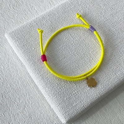 Pulseira amarela com pendente de trevo dourado sobre tecido branco texturizado