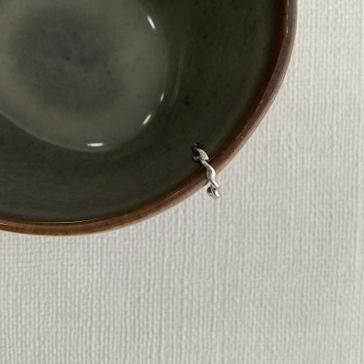 Taça de cerâmica cinza com borda castanha e ornamento metálico em nó