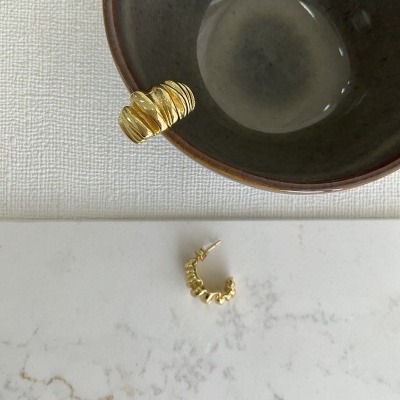 Dois brincos dourados de aro texturizados ao lado de uma tigela cinza