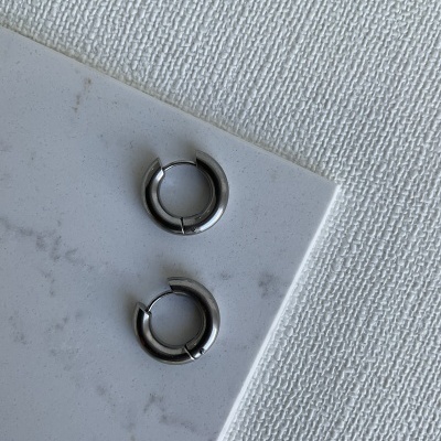 Dois brincos de argola pequenos em metal prateado sobre superfícies brancas texturizadas