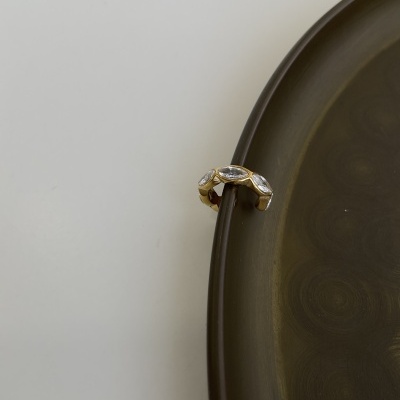 Anel dourado com pedras transparentes sobre borda de prato escuro