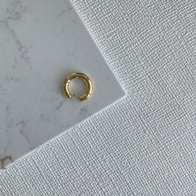 Argola dourada pequena sobre superfície branca de mármore e tecido branco texturizado