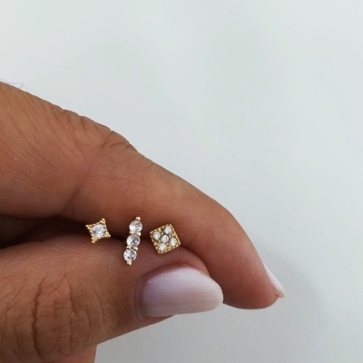 Brincos dourados pequenos com pedras brilhantes segurados por uma mão