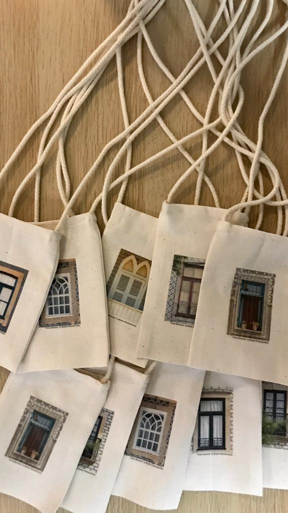 Bolsa Telemóvel "Uma janela do Porto" Pequenas bolsas de tecido cru com ilustrações de janelas, com cordões finos, sobre madeira clara.