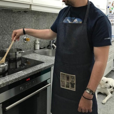 Homem a cozinhar com avental preto e cão branco no chão